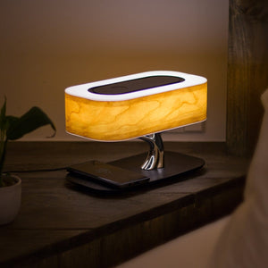 Demonstration of Light Of Tree table lamp on a bedside table with a phone charging and playing music with the lights on.