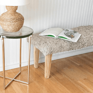 Handwoven Textured Taupe Bench with Wood Legs besides of Glass Table in Gold and Rose color. 