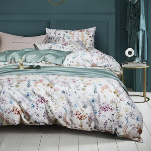 Artemis floral duvet cover set with white background and green sheets; there is a bedside table with some magazines and a lamp.