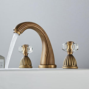 Antique color three whole Samira Bathroom Faucet on white sink with transparent handles.