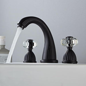 Black three hole bathroom tap with transparent handles on white bathroom sink. 