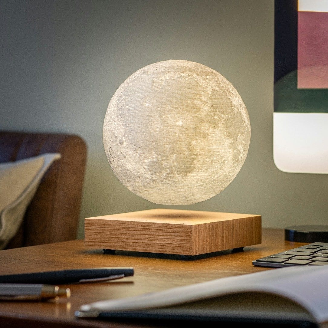 White Ash floating moon lamp on a wooden bedside table with glasses and notebooks.