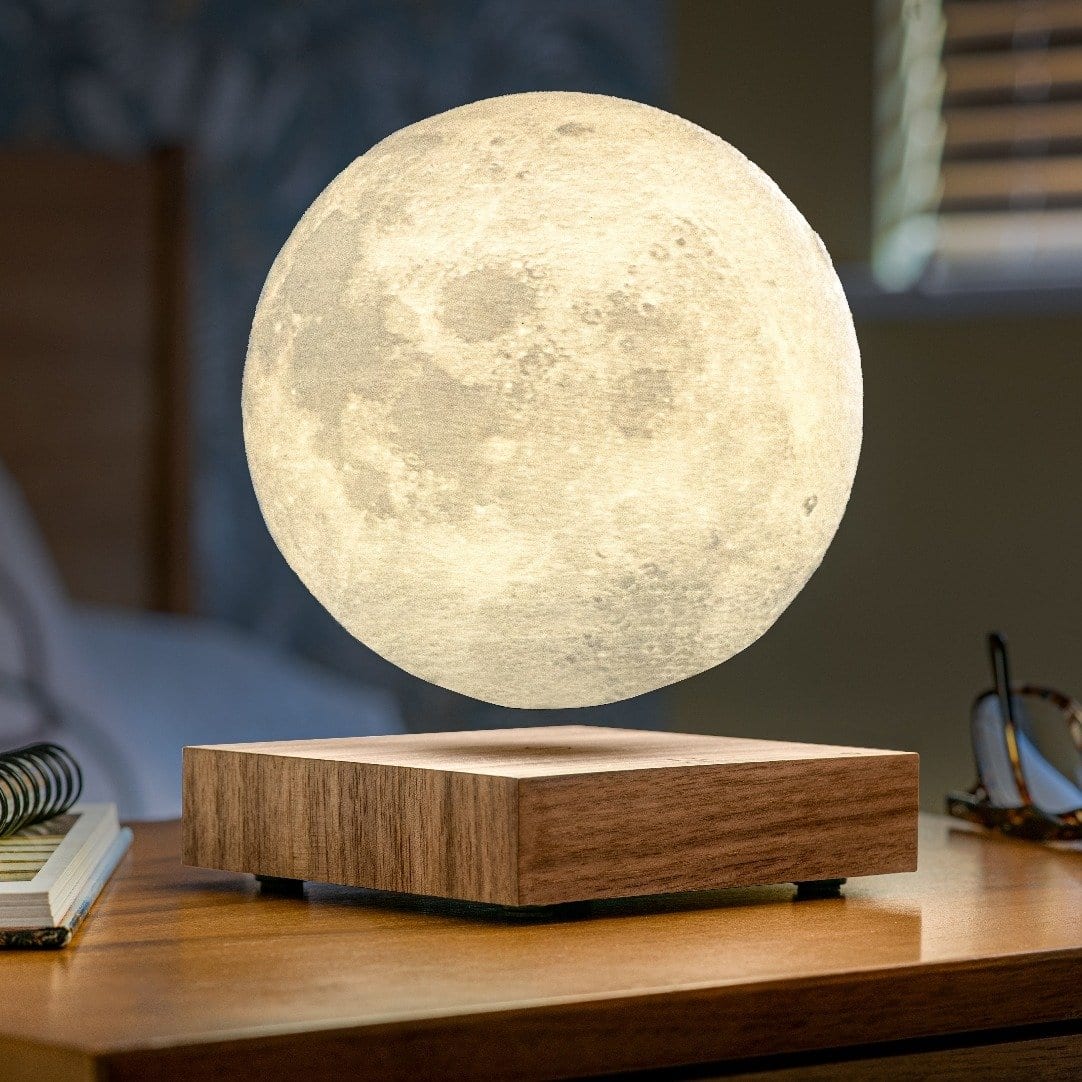 White Ash floating moon lamp on a wooden bedside table with glasses and notebooks.