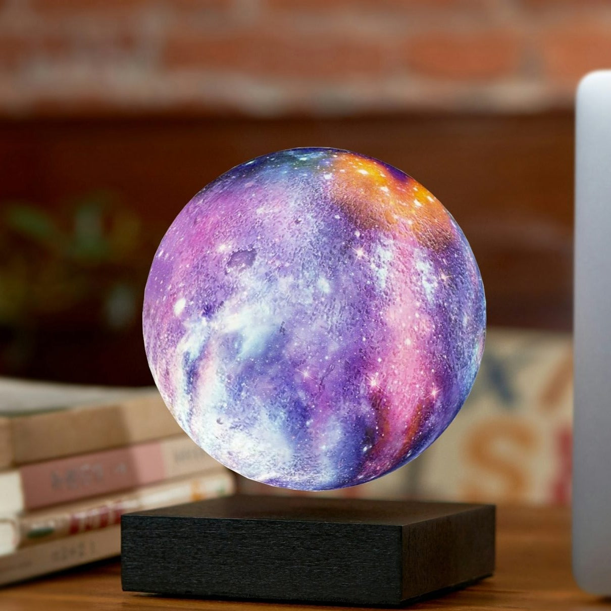 Floating galaxy lamp by Gingko on a walnut color desk besides a Macbook Pro
