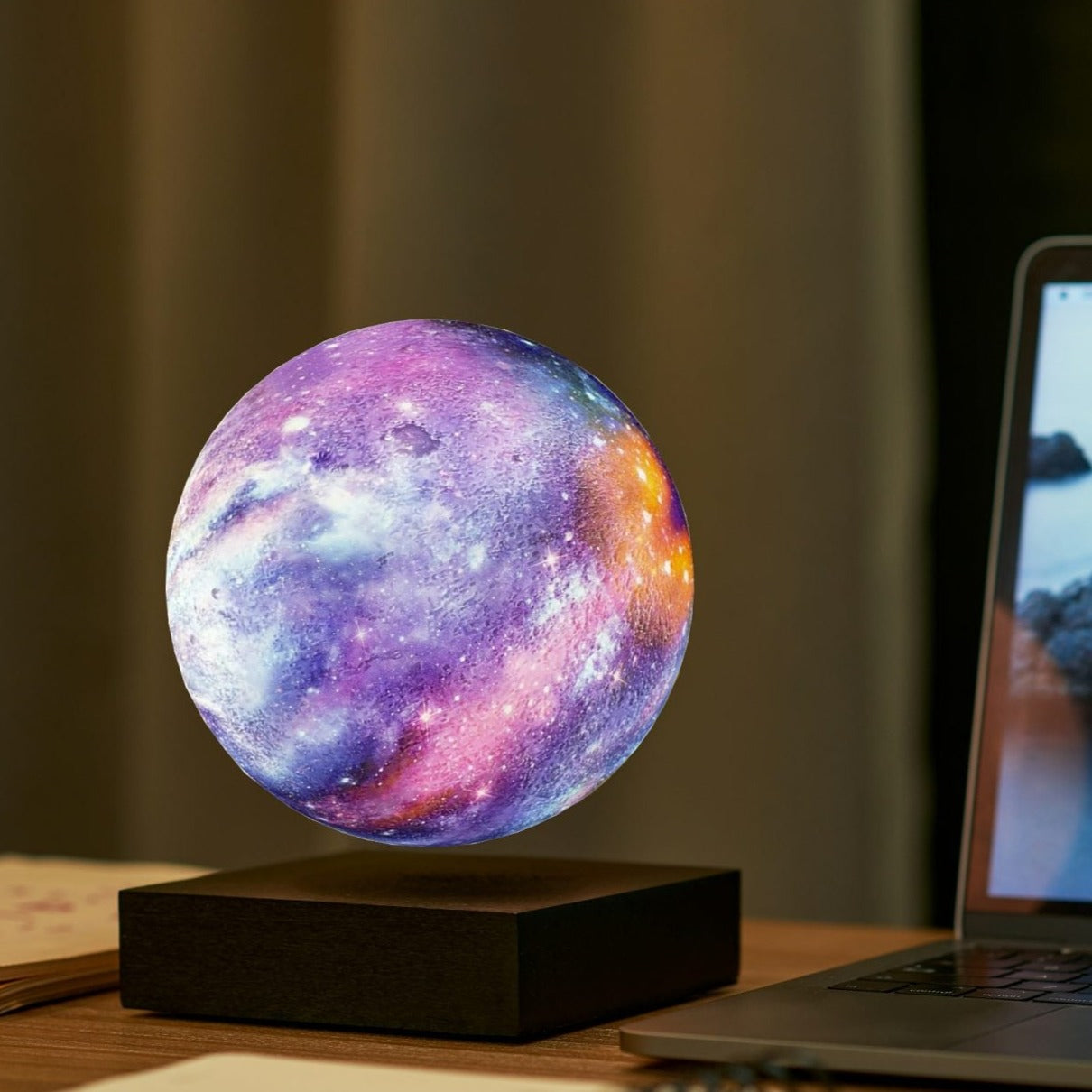 Floating galaxy lamp by Gingko on a walnut color desk besides a Macbook Pro