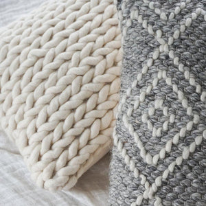 Handwoven white pillow on a bed with a grey color handwoven throw pillow.