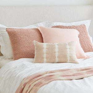 Pink Knotted Texture Cotton Throw Pillow on a bed with white bed sheets and more throw pillows.
