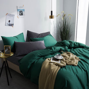 Corner view of Grace Silk Green Duvet Cover Set in minimalist bedroom. The bedding set comes with two pillowcases, the duvet cover, and the flat bed sheet.