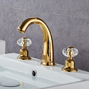 Gold color bathroom tap with three holes on a white bathroom sink.