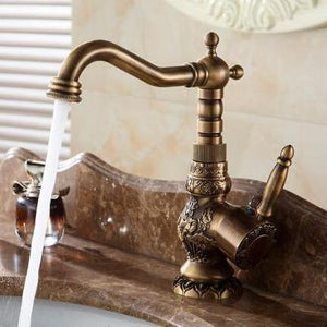 Antique Brass Bathroom Faucet with open water flow on a marble bath sink.
